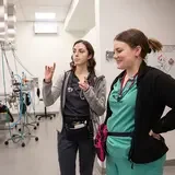 Two medical clinic staff stand in the exam room having a lively discussion