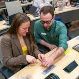 Veterinary students sit at a desk in a large lecture oom learning various animal techniques