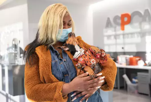 woman with small dog stands smiling in clinic near aspca signage