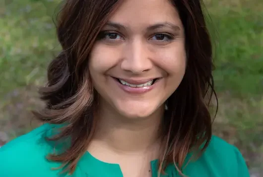 Headshot of Kate Meghji wearing a green top against trees