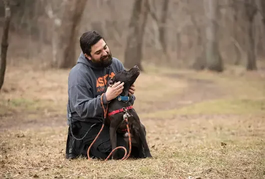 Man in ASPCA sweatshirt petting black dog in field