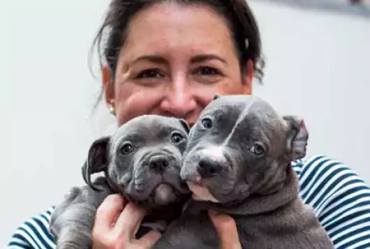 smiling woman holds two puppies