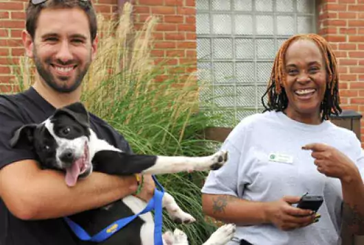 man holding dog and woman outside shelter smiling and laughing