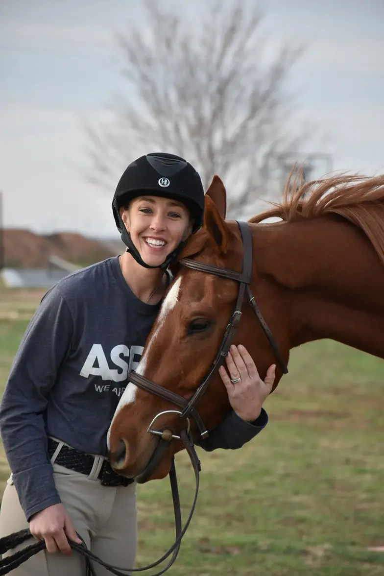 woman in helmet hugs her horse
