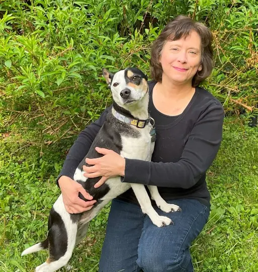 headshot of dr makolinski kneeling on green grass hugging her black and white dog