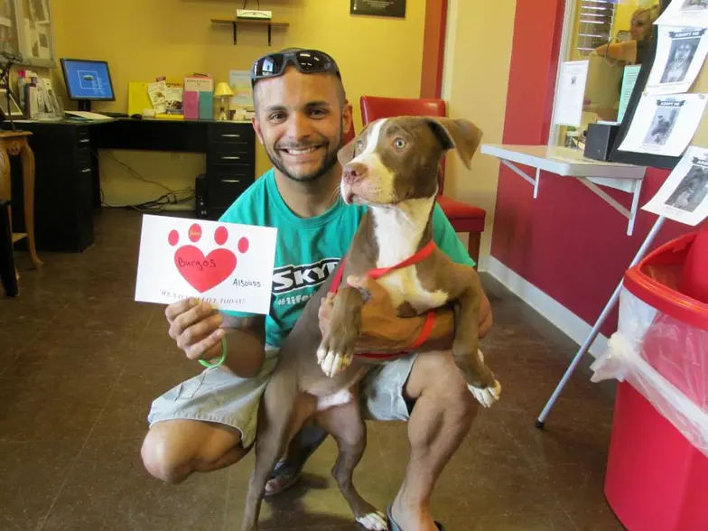 Man crouched down with one arm around dog and the other holding up a sign with a heart on it