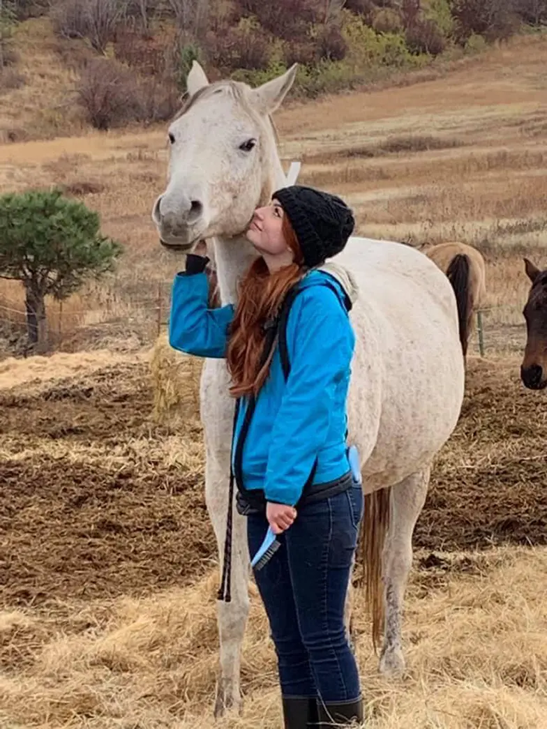 girl stands looking at white horse lovingly