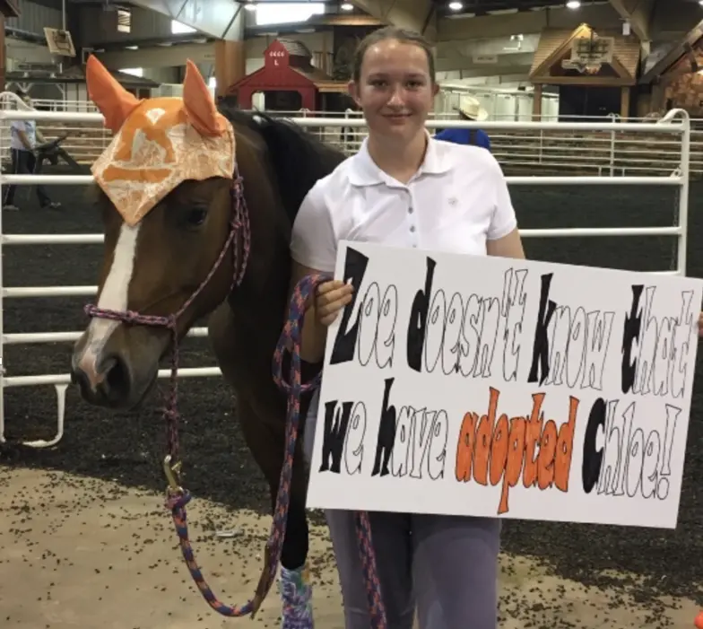 Zoe Page with her horse Chloe and a sign revealing Chloe's adoption